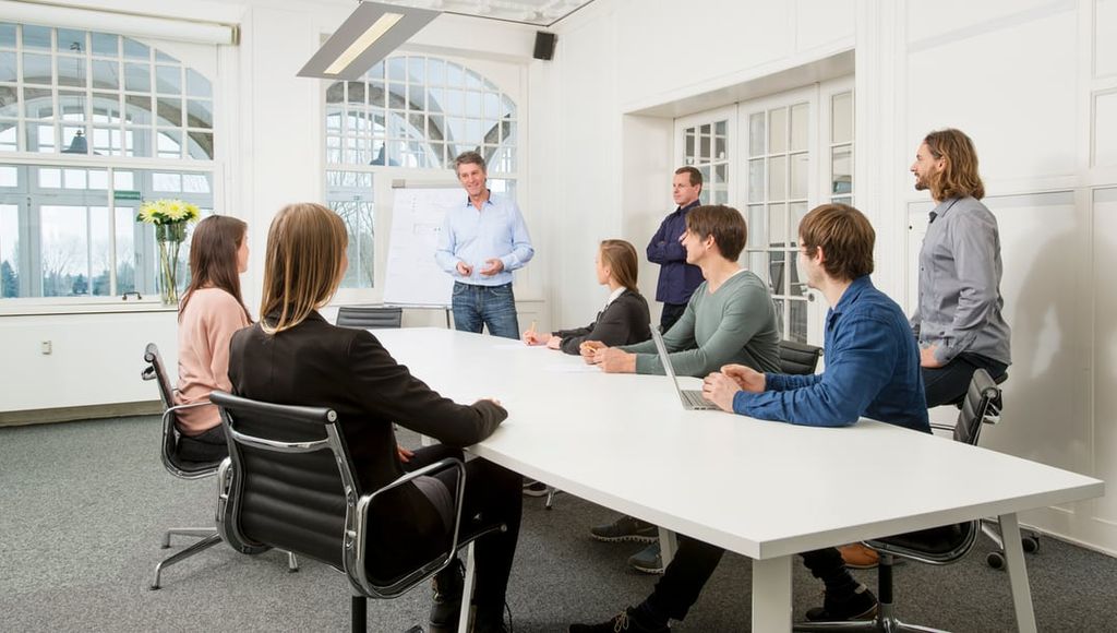 Heller, moderner IPN-Büroraum in Köln — Natursteinwände, hohe Rundbogenfenster, Pflanzen und gemütliche Sitzecken.